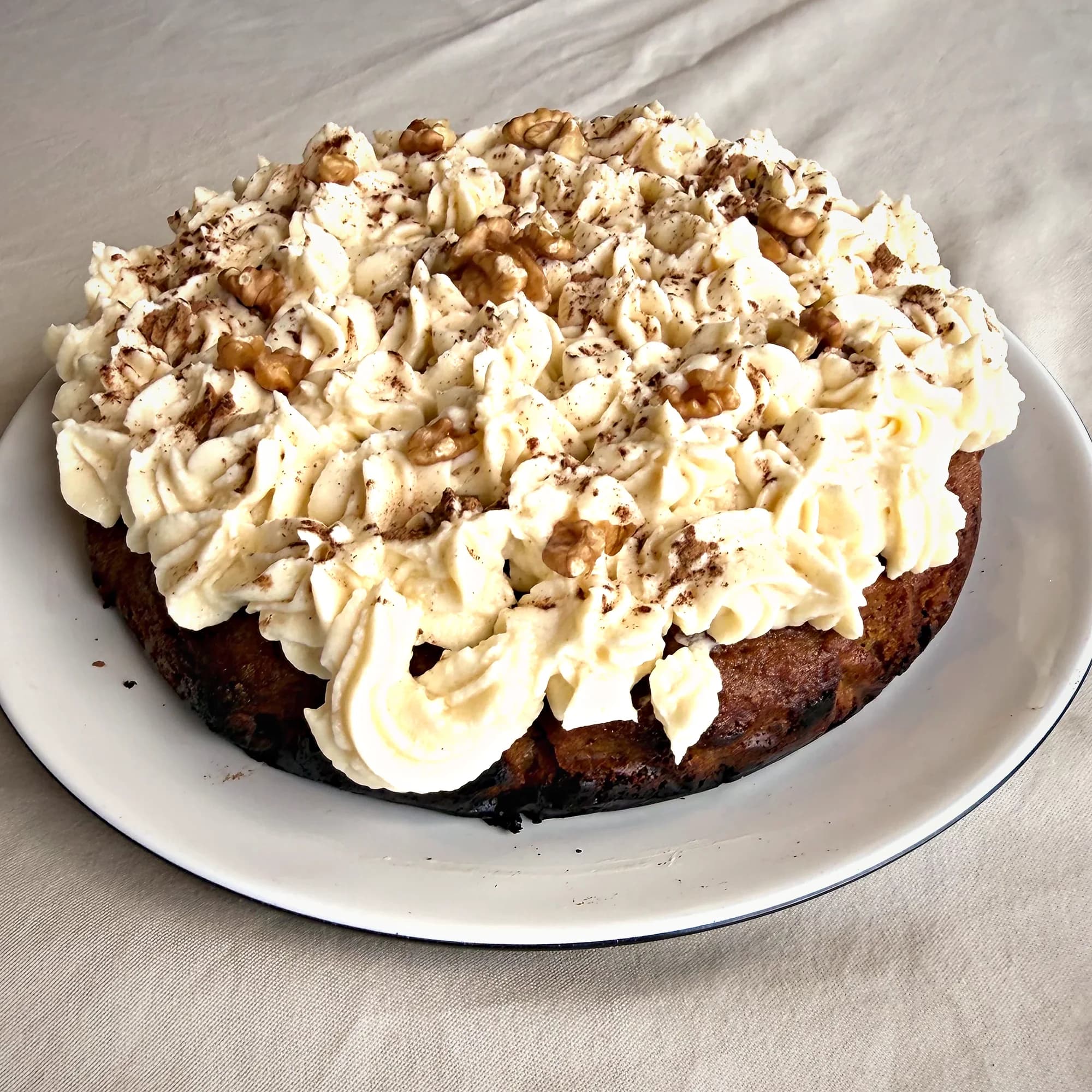 A whole cake finished with piped cream frosting and walnuts